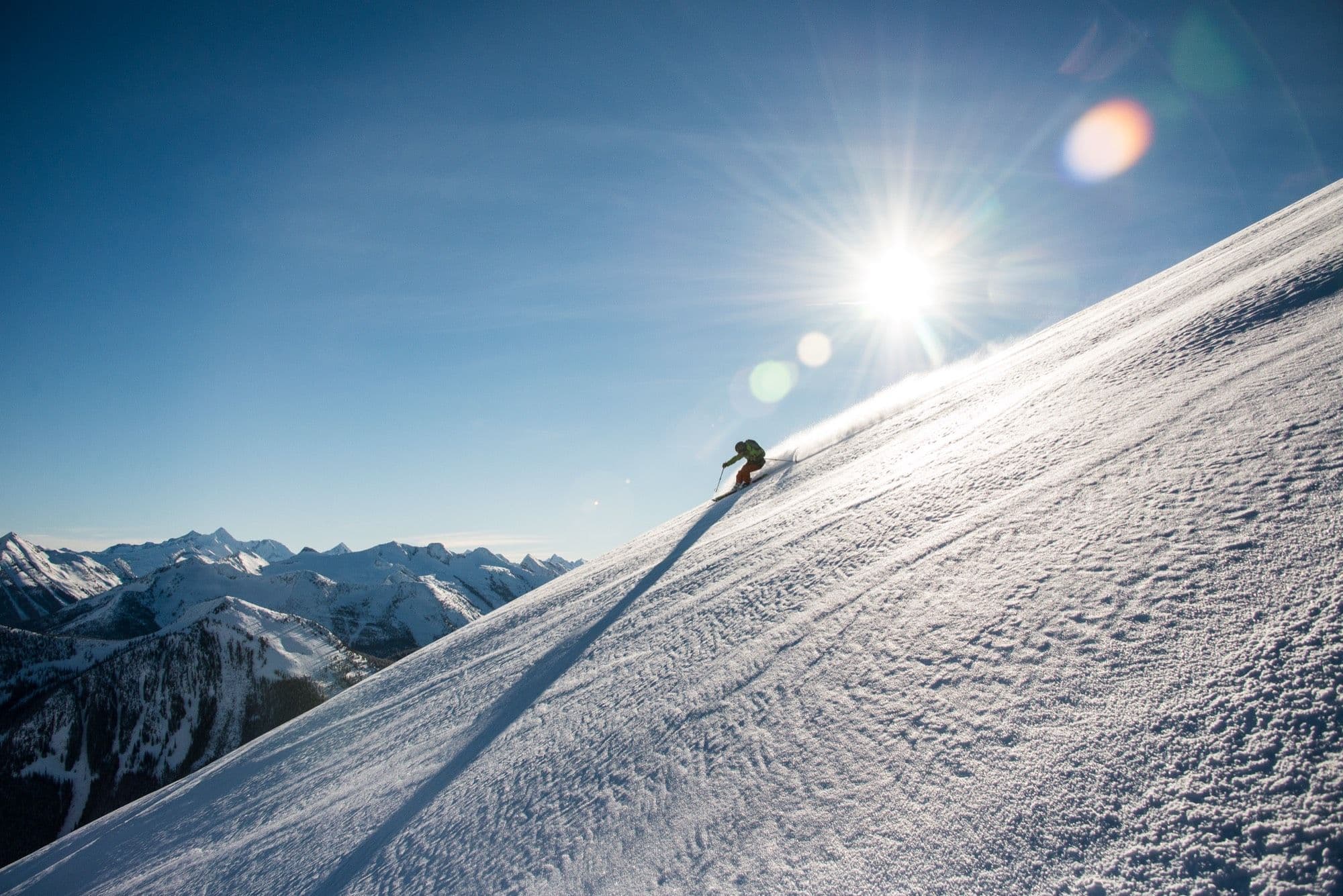 A CMH guest skiing a sunlit alpine slope in British Columbia
